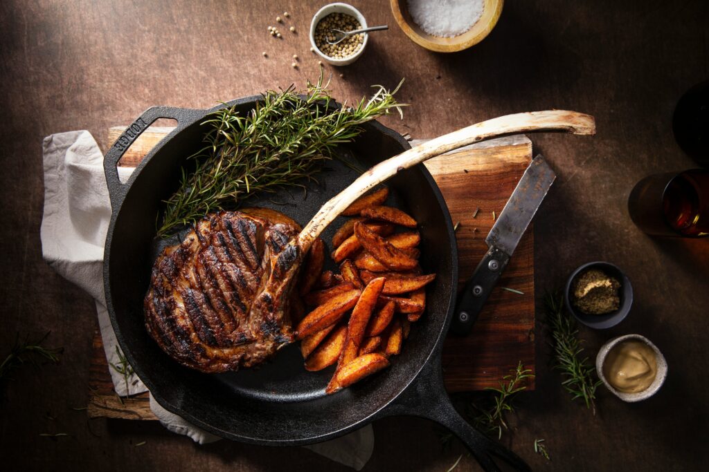A delicious tomahawk steak resting in a skillet with herbs and fries