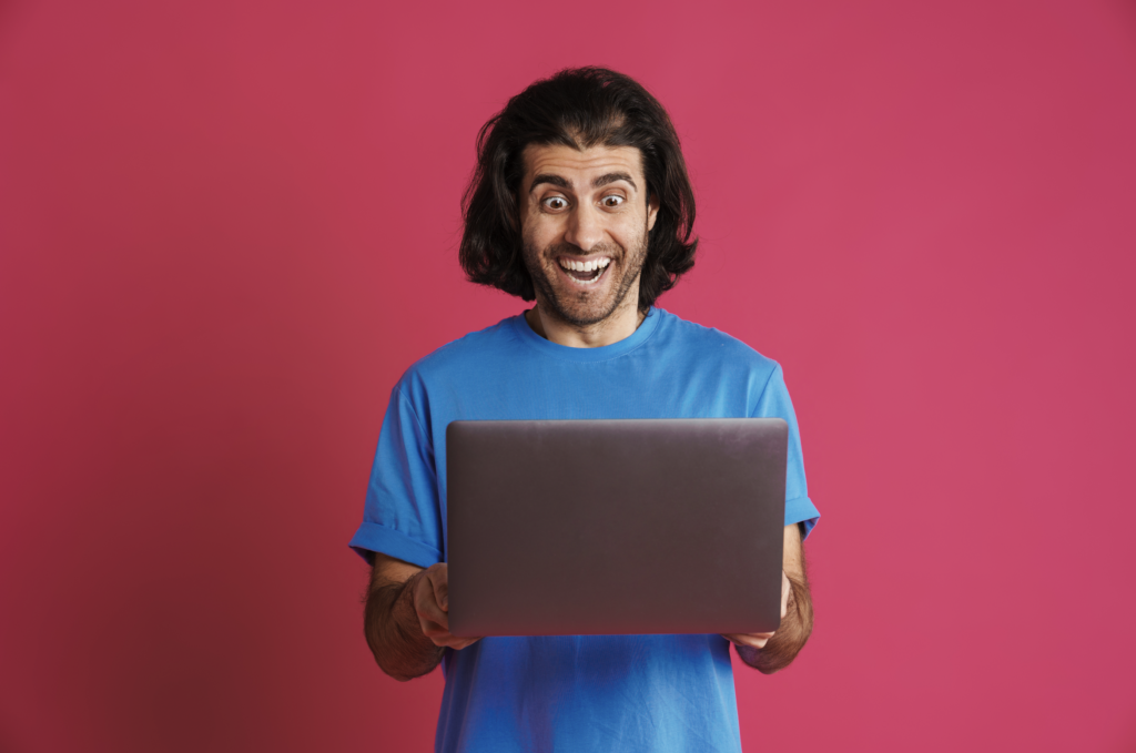 Excited man holding a laptop in front of a red backdrop.