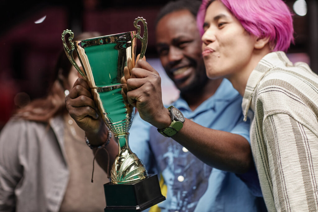 Group of friends smiling while proudly holding trophy together. Expressions of joy and camaraderie captured perfectly in moment of achievement with diverse friends