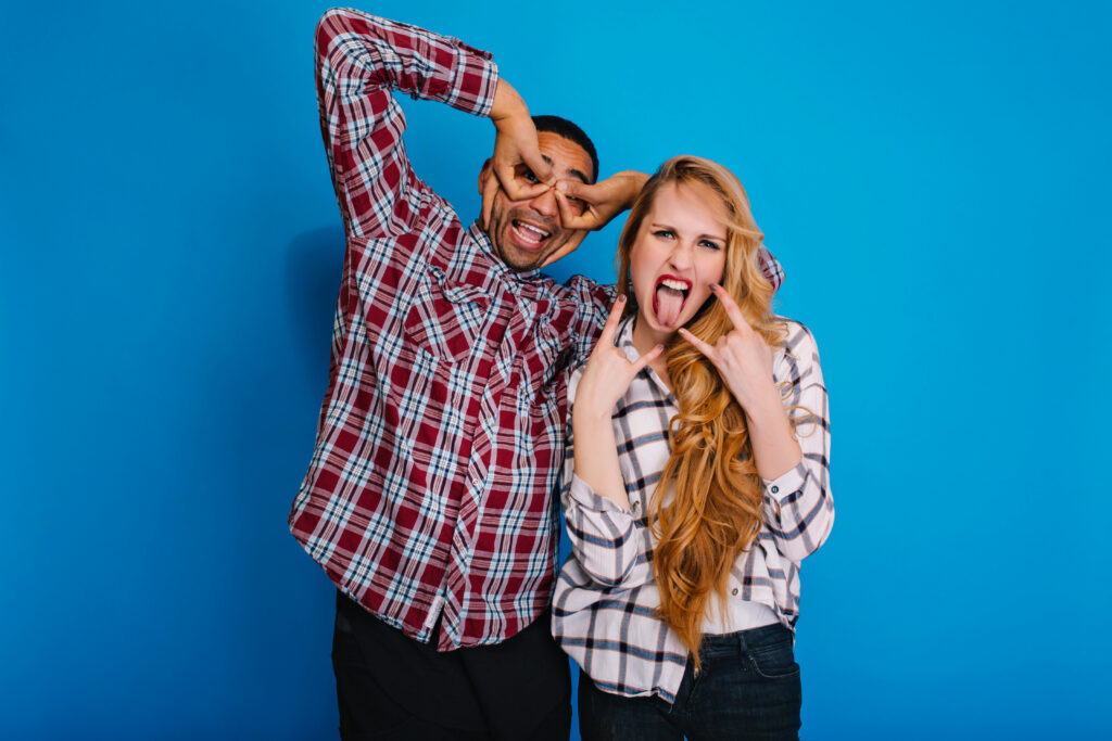 Portrait funny moments of excitedcouple fooling around to camera on blue background. Having fun, weekends, showing tongue, relaxing, brightful emotions, expressing true positive emotions