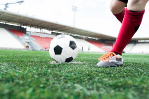 Low angle action shot of unrecognizable teenage boy forcefully kicking ball during football match on outdoor stadium, copy space