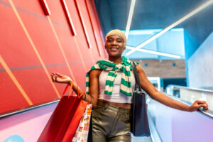 Urban african woman standing on escalator carrying shopping bags and smiling at camera