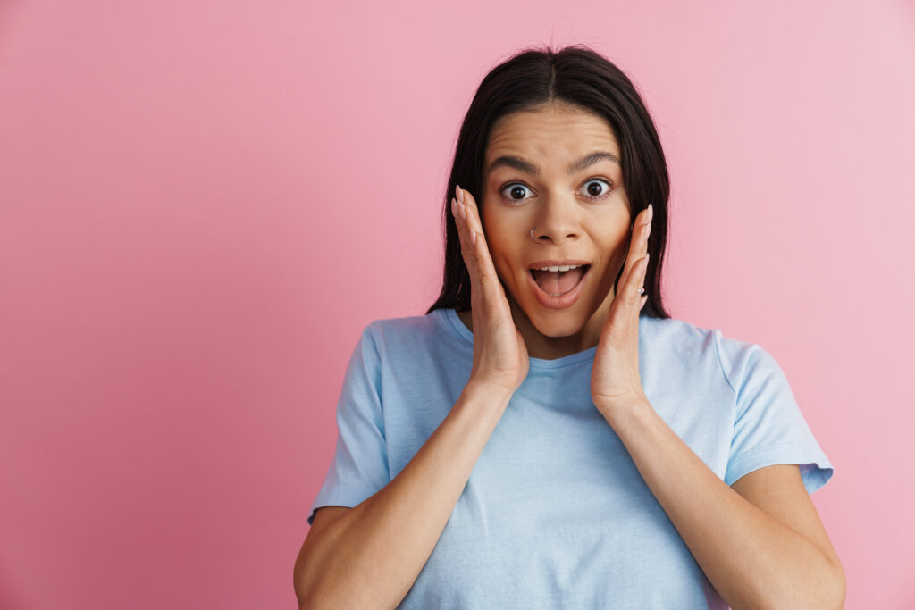 Young hispanic excited woman expressing surprise at camera isolated over pink wall