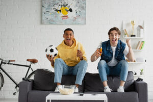 young interracial football fans sitting on couch and celebrating